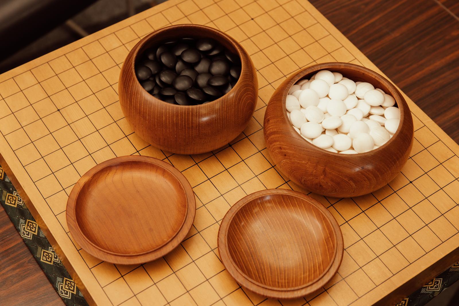 木製の碁笥に詰まった黒石と白石が黄色い碁盤に並ぶ囲碁セット