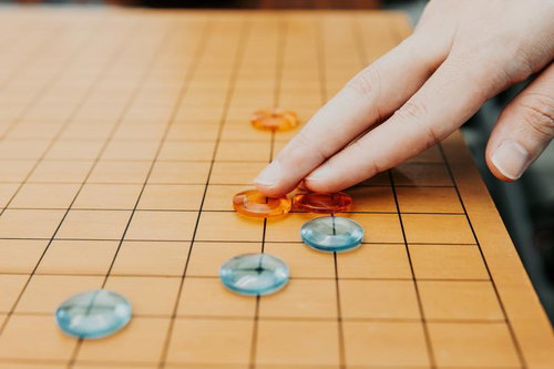 アクリル製の碁石で対局する手、九路盤の上での一手
