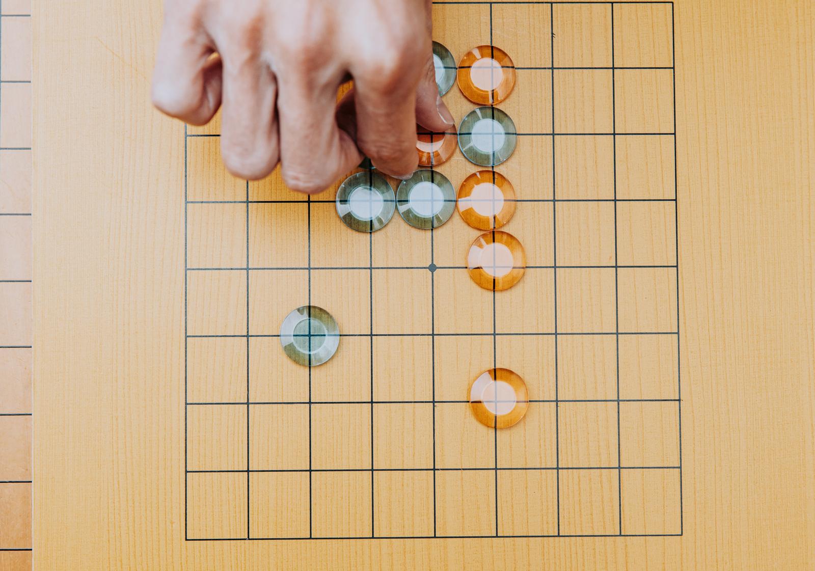 九路盤の上で白と琥珀色のおはじき碁石を並べてゲーム中の写真