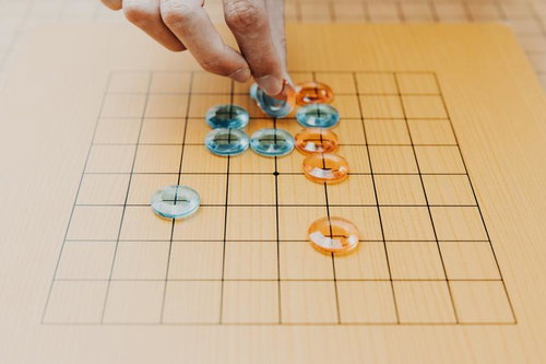 木製の九路盤に置かれたアクリル製の碁石を手で動かす