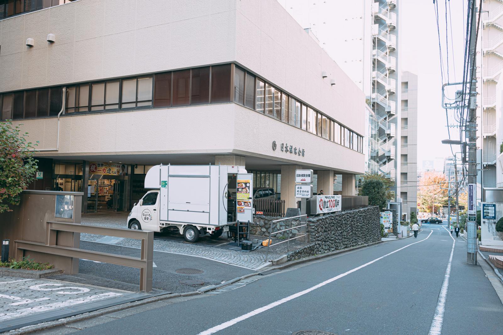日本棋院前の帯坂。白い建物と石畳の道、配送車が停車している