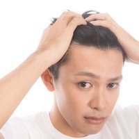髪をかきあげておでこと生え際を見せる男性の写真