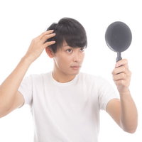 手鏡で薄毛・生え際のヘアチェックをする若い男性の写真