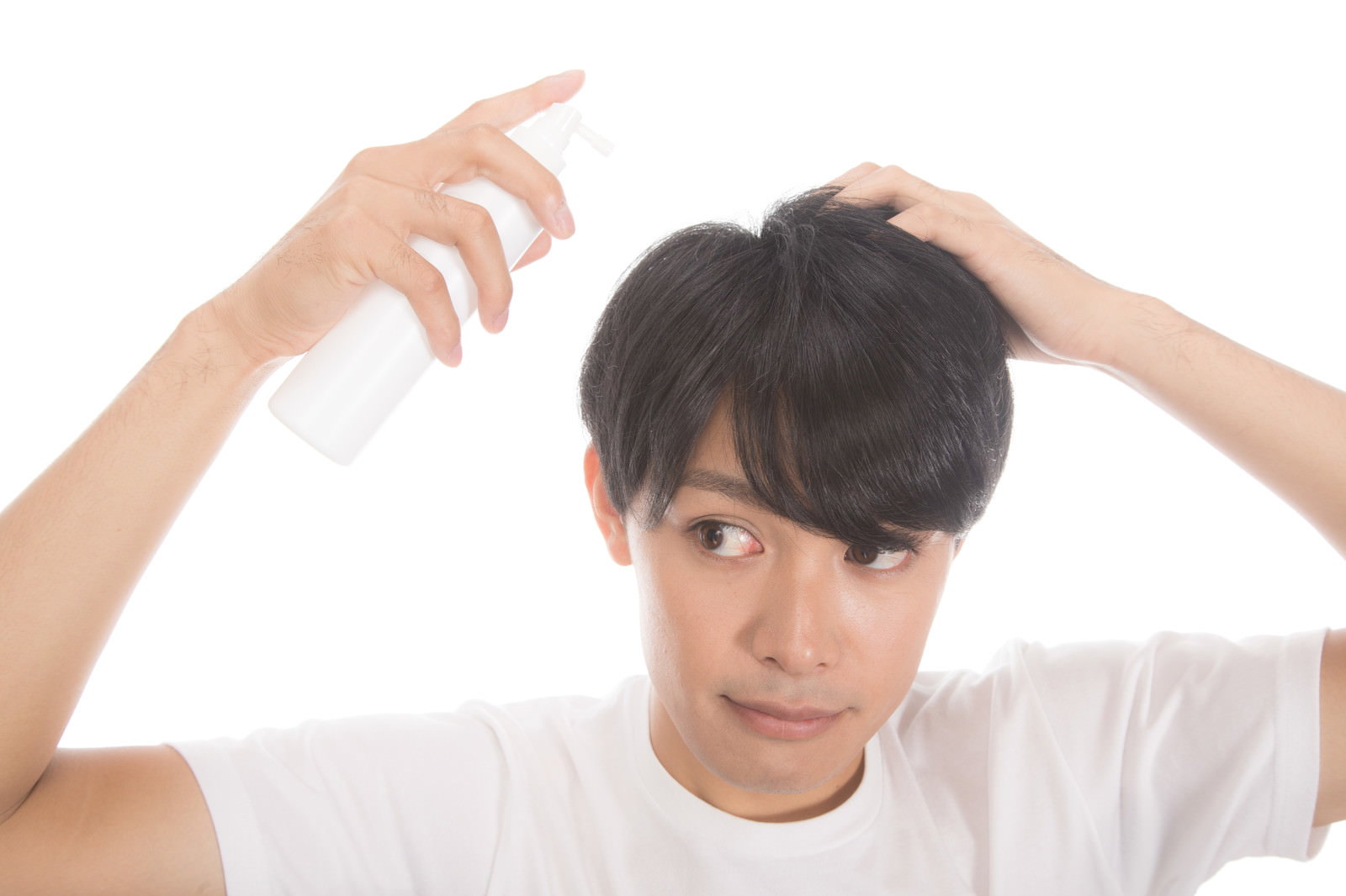 白いシャツを着た若い男性が両手で増毛スプレーを髪に使用している［モデル：完伍］