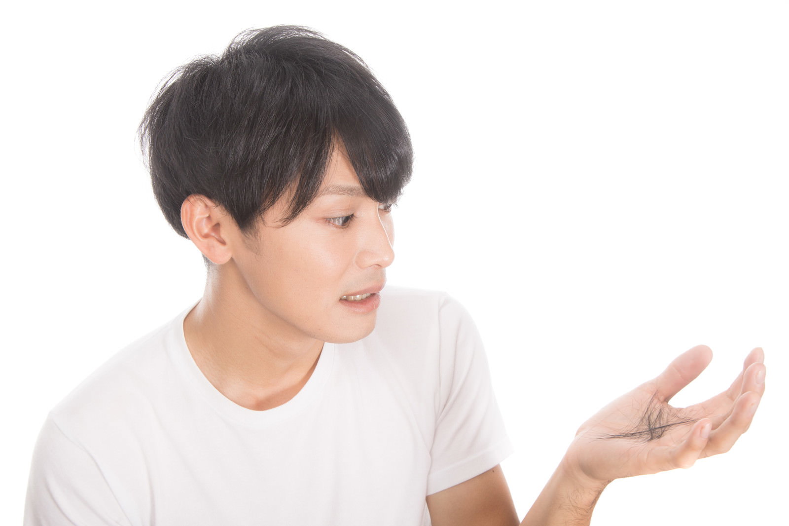 手のひらを見つめて抜け毛を気にする白いTシャツの若い男性［モデル：完伍］