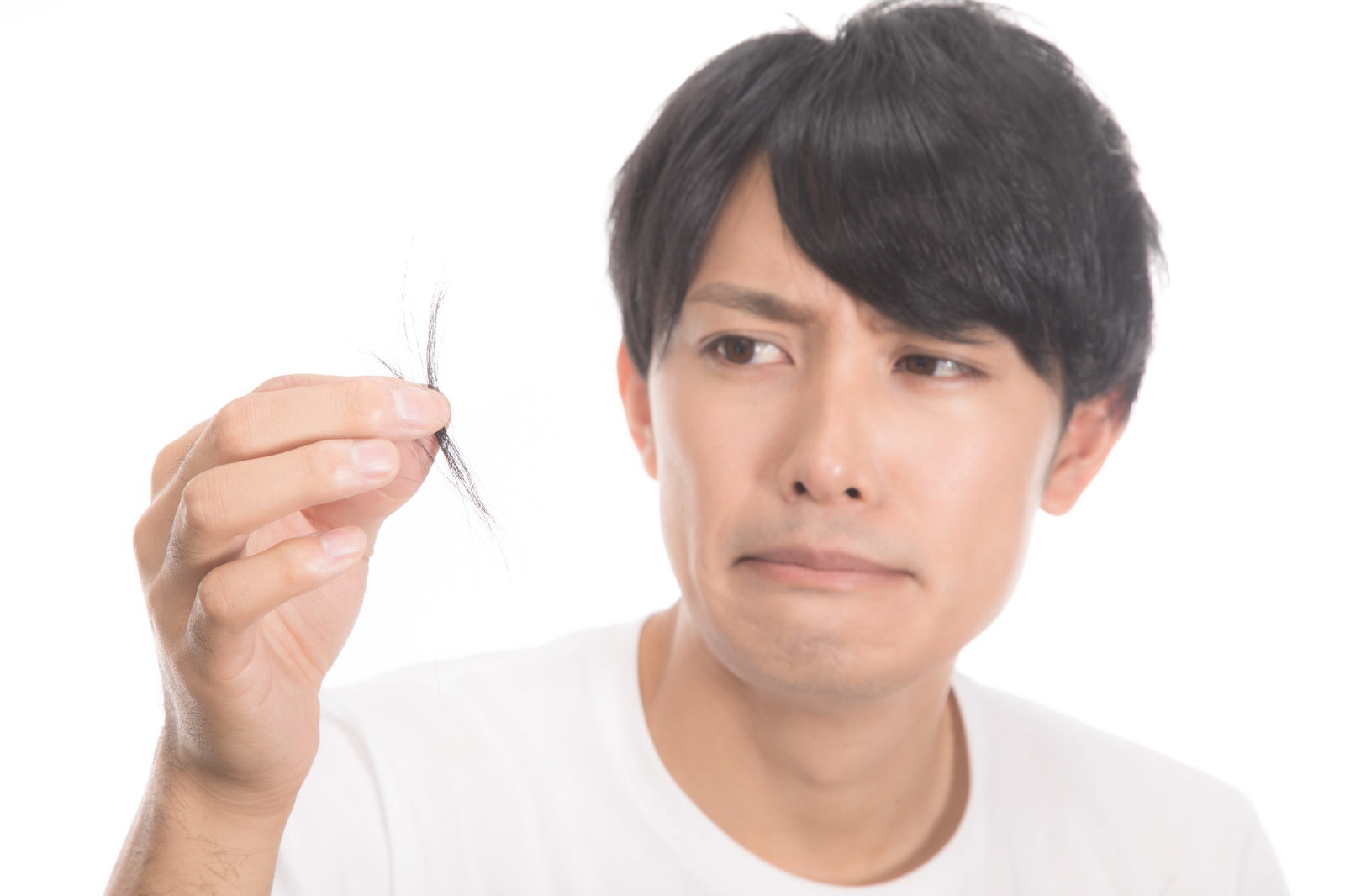 髪の毛を手に持ち心配そうな表情を見せる白いTシャツの若い男性［モデル：完伍］