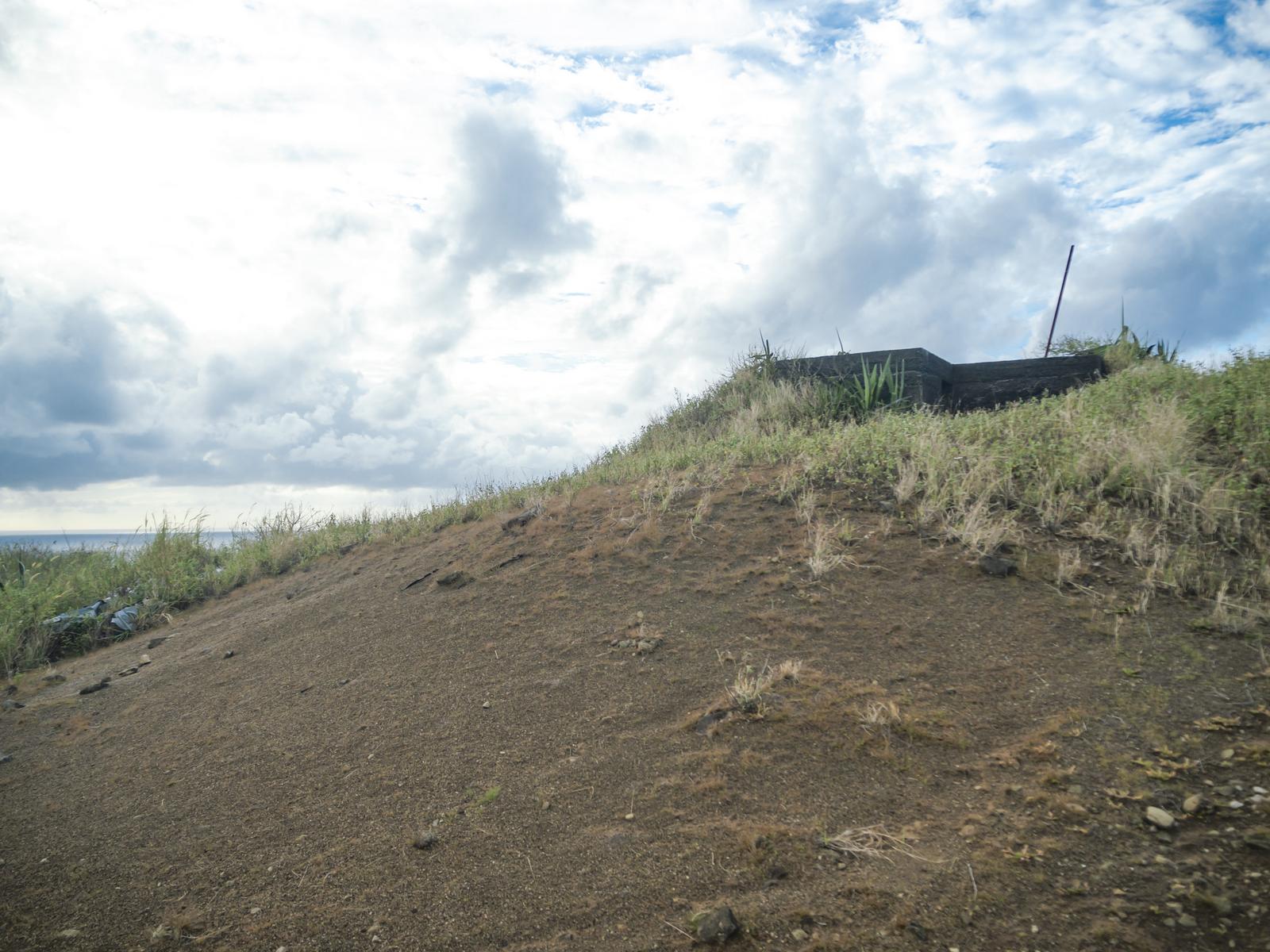 硫黄島の丘に建つ米軍IWOパブの建物と雑草、曇り空と水平線