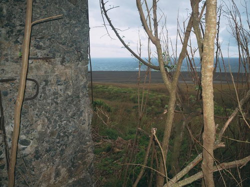 鉄筋が露出した砲台の壁の横から見る翁浜（上陸海岸）