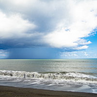 翁浜から見る海面に降りるスコールの柱と南硫黄島の写真