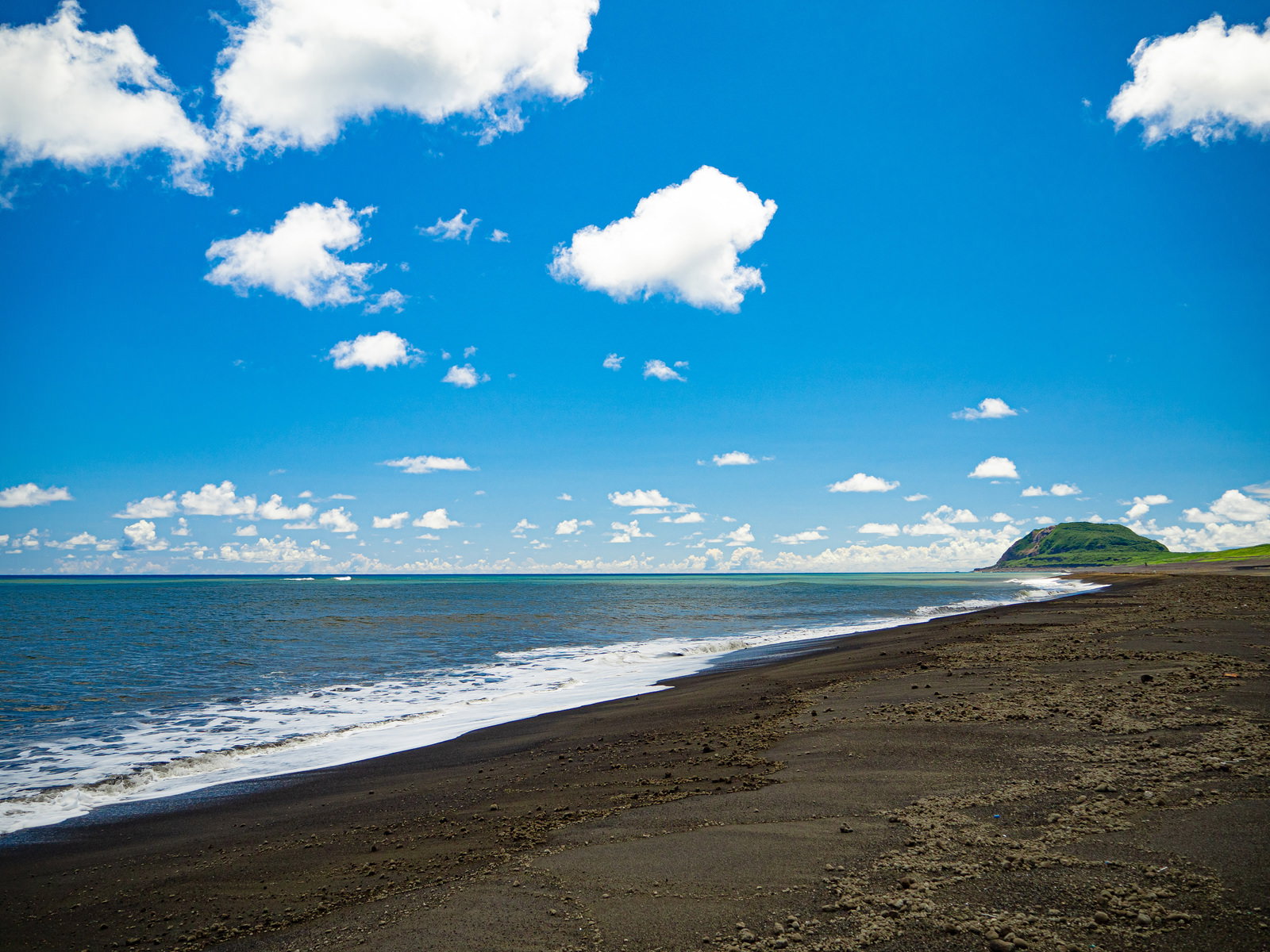 硫黄島の翁浜海岸に軽石が流れ着き、背景に摺鉢山が見える風景