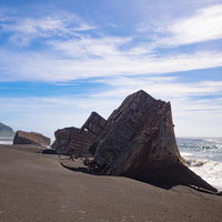 ▲千鳥ヶ浜に横たわる朽ちたコンクリート船の瓦礫と遠くに見える摺鉢山の写真
