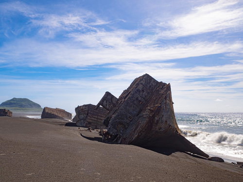 ▲千鳥ヶ浜に横たわる朽ちたコンクリート船の瓦礫と遠くに見える摺鉢山の写真