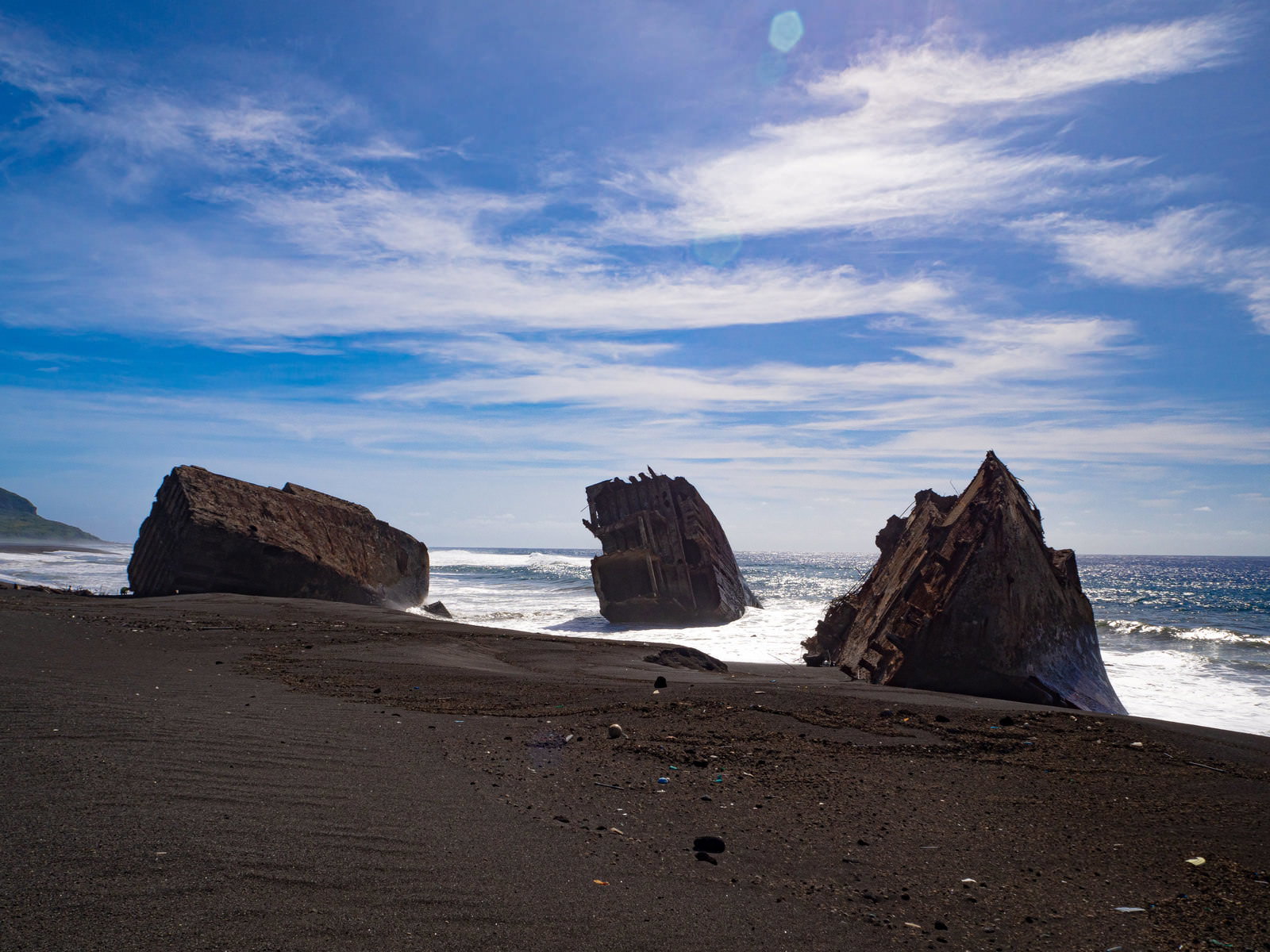 Three shipwreck remains on a black sand beach with white waves