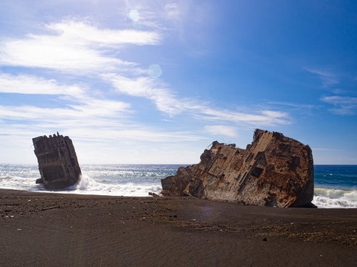 南国の太陽にきらめく波に洗われるコンクリート船の残骸