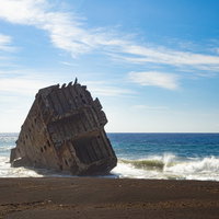 キラキラと光る波が寄せる硫黄島・千鳥ヶ浜のコンクリート船の残骸の写真