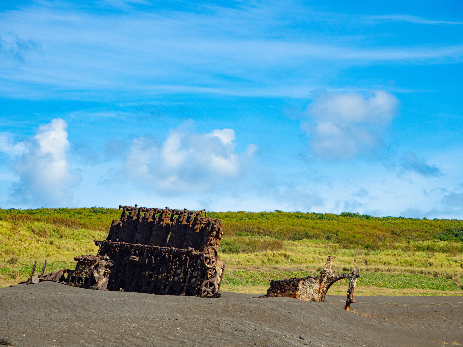 硫黄島の黒い砂浜に露出した沈船のエンジンと錆びた瓦礫