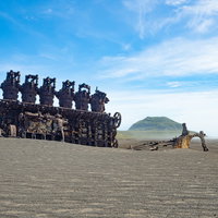 千鳥ヶ浜に聳え立つ錆びついた船のエンジンと向うに見える摺鉢山の写真