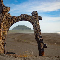 サンゴが残る瓦礫の向うに見える摺鉢山と広がる砂浜と波が寄せる海の写真