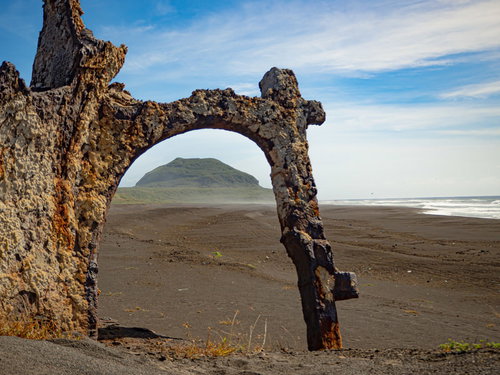 サンゴが残る瓦礫の向うに見える摺鉢山と広がる砂浜と波が寄せる海