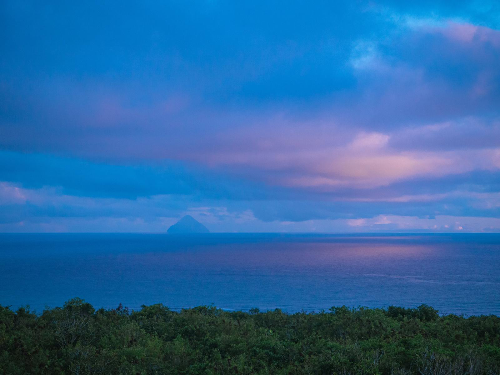 夕暮れ時、紫とピンク色に染まる海の先に見える南硫黄島のシルエット