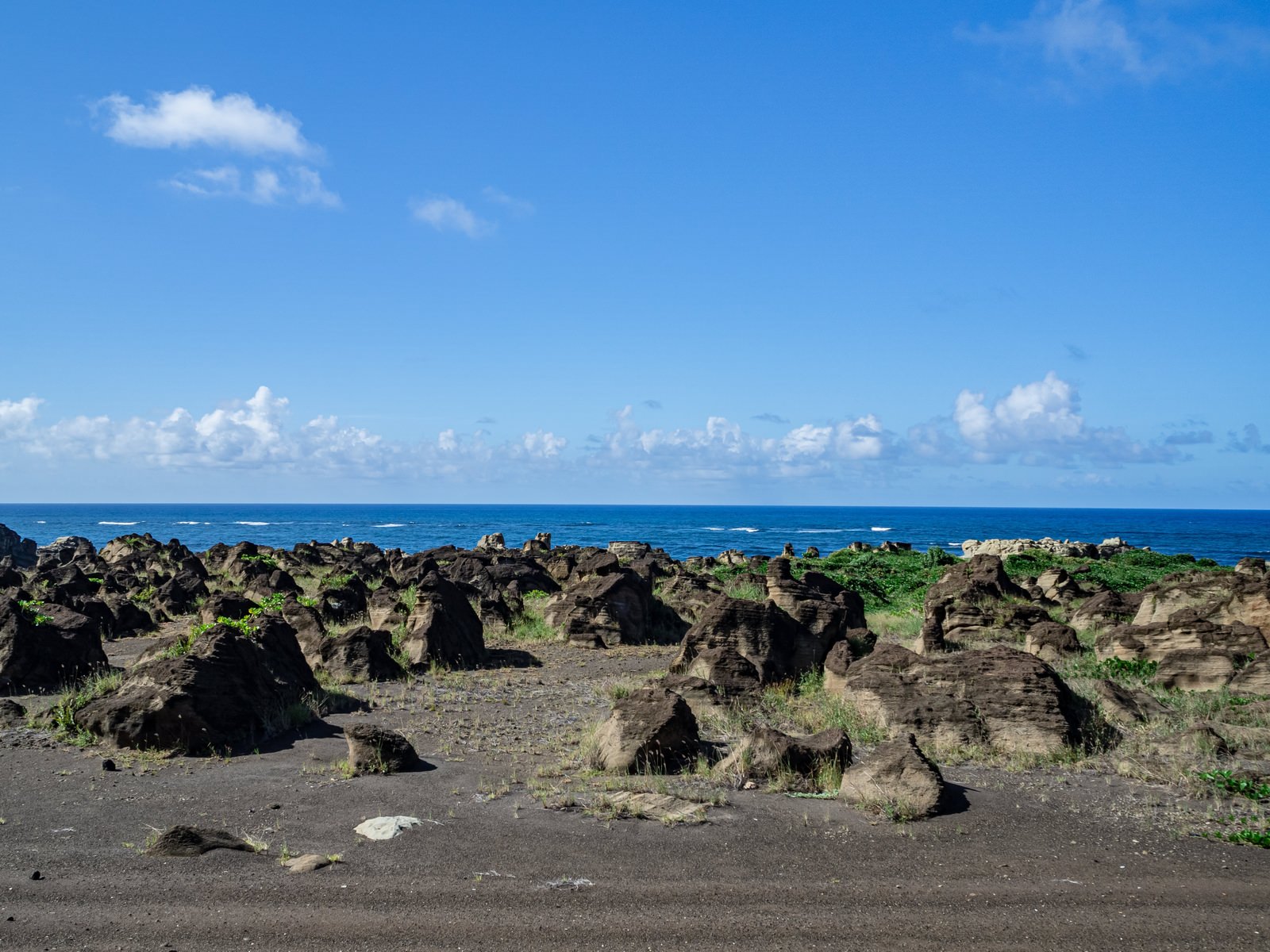青い海と空の下、黒っぽい岩石が海岸線に点在する北の鼻の海岸風景