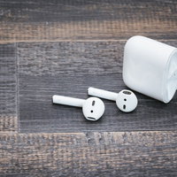 白色のワイヤレスイヤホンと充電ケース、木目調背景の写真
