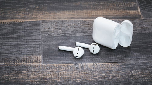 白色のワイヤレスイヤホンと充電ケース、木目調背景