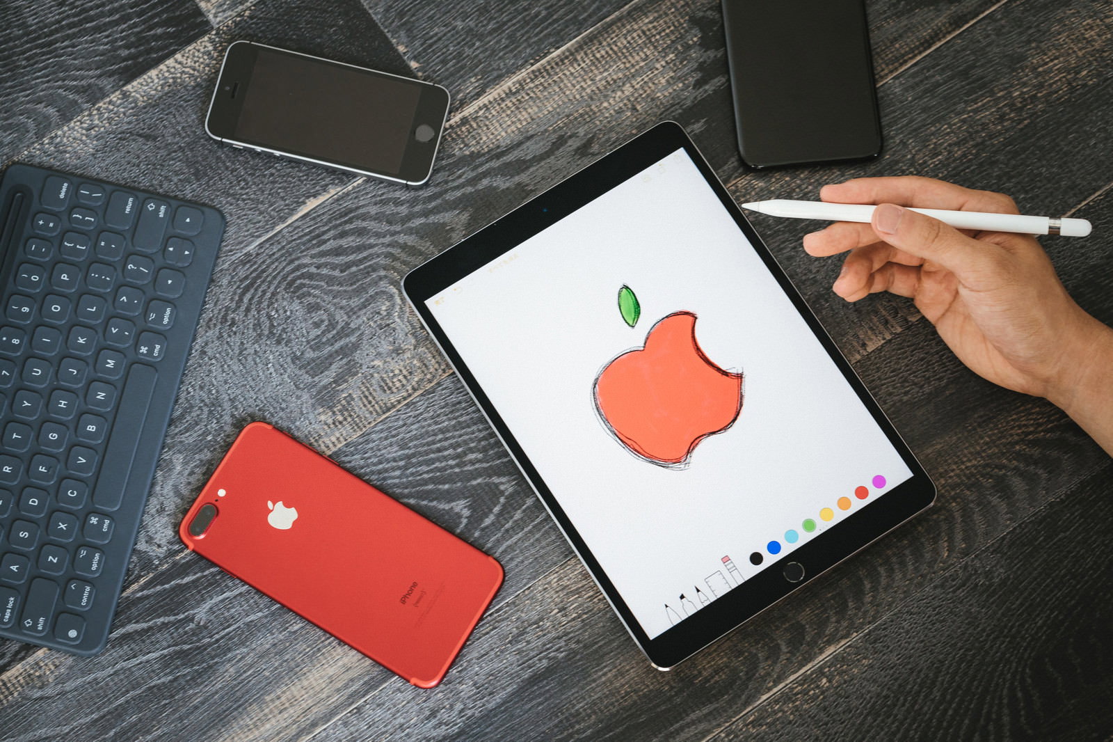白いタブレット画面に赤い林檎マークを描く右手とスタイラスペン