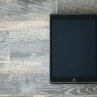 木目の床に置いた大きさが異なるタブレットを重ねるの写真