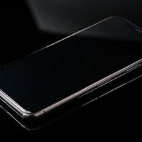 黒いテーブルに置かれたiPhone Xと映り込む照明の光の写真
