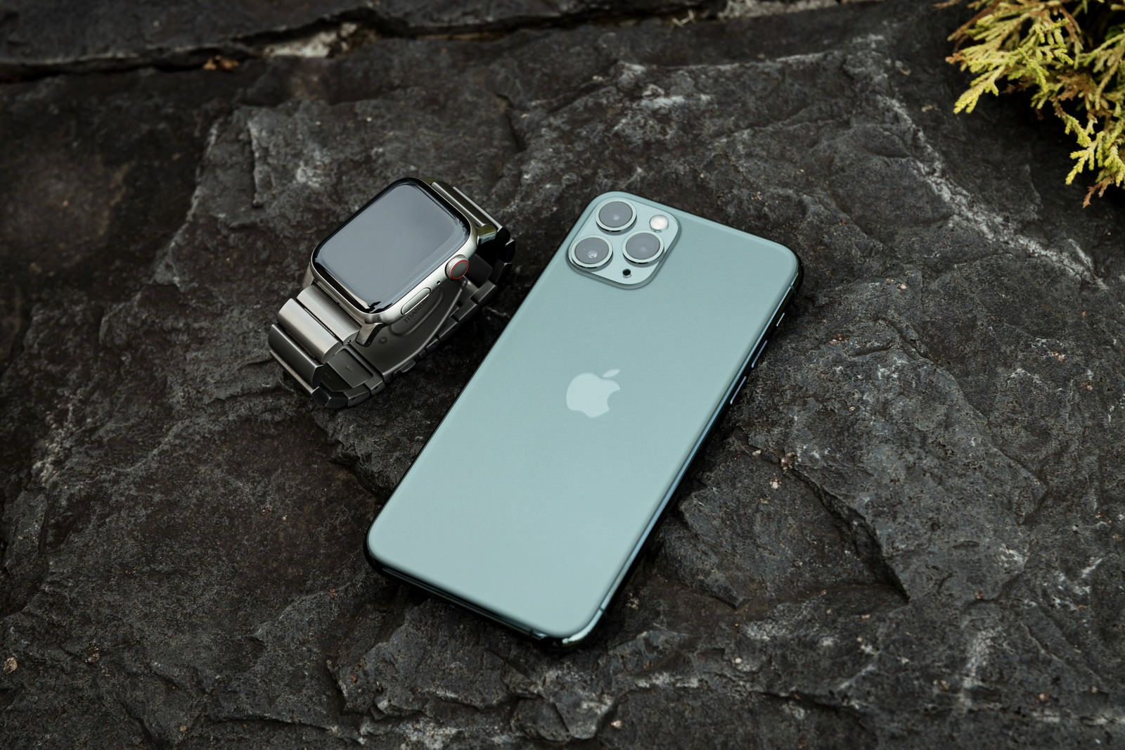 石の上に置かれた黒いApple WatchとブルーグリーンのiPhone 11 Pro