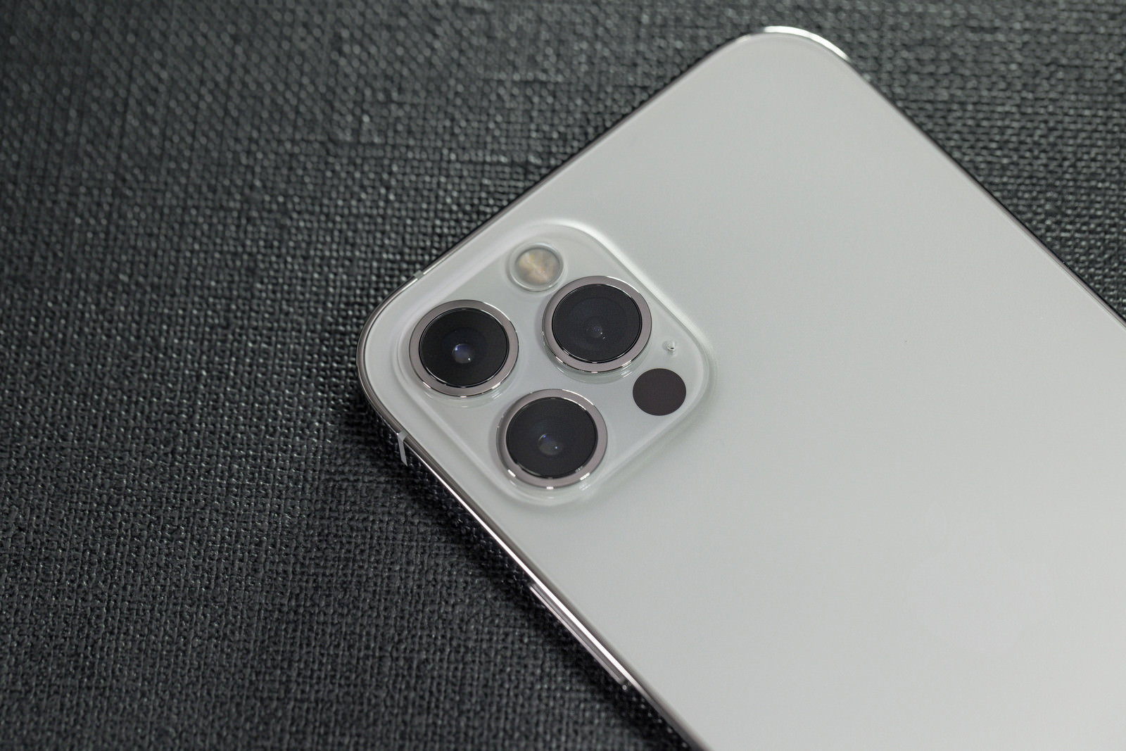 グレーの背景に置かれたホワイトのiPhone 12 pro、3眼カメラレンズが特徴的