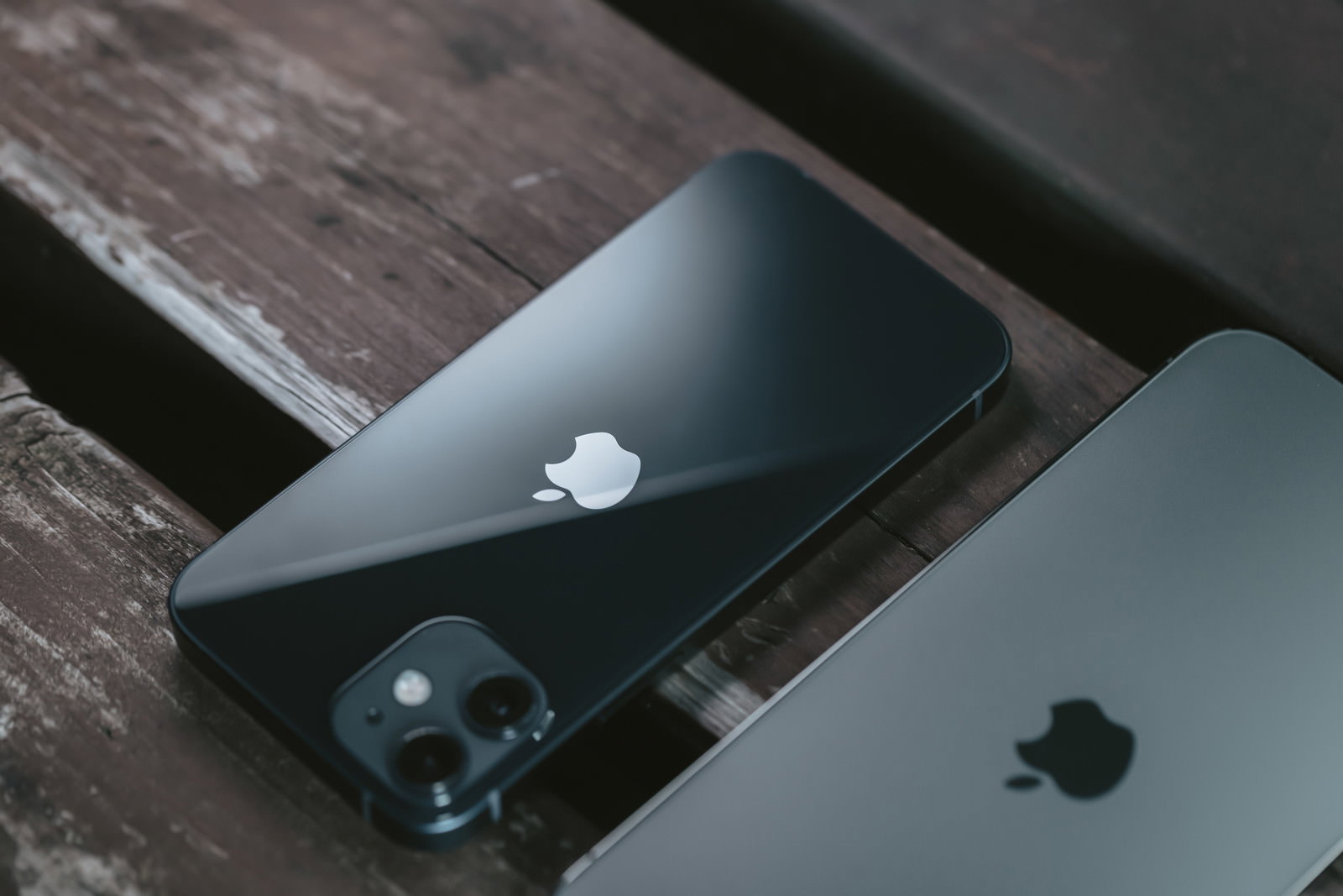 木目調の表面に置かれた黒と白のiPhone 12の背面