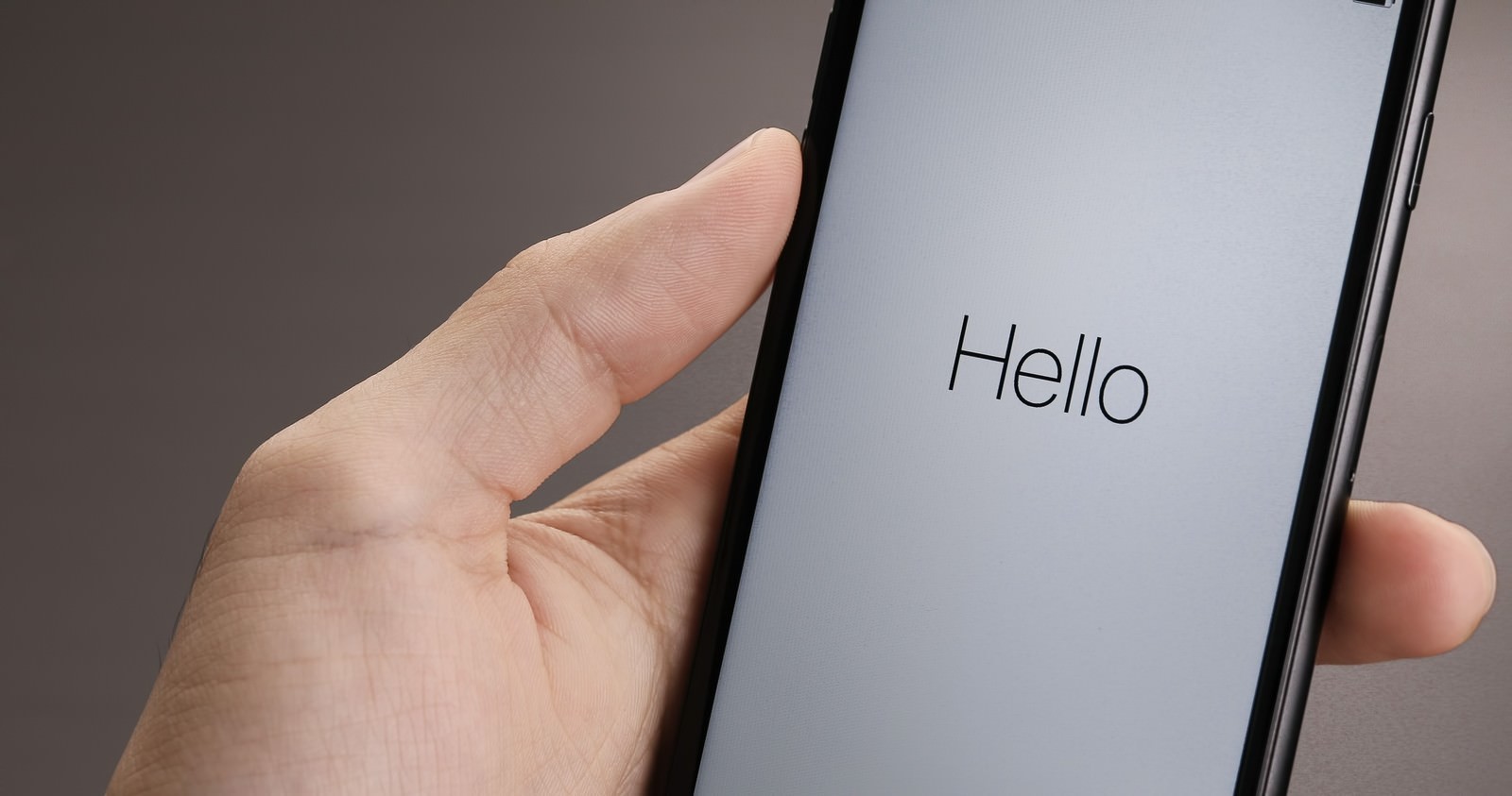 「Hello」と表示されたスマートフォンを手で持つ