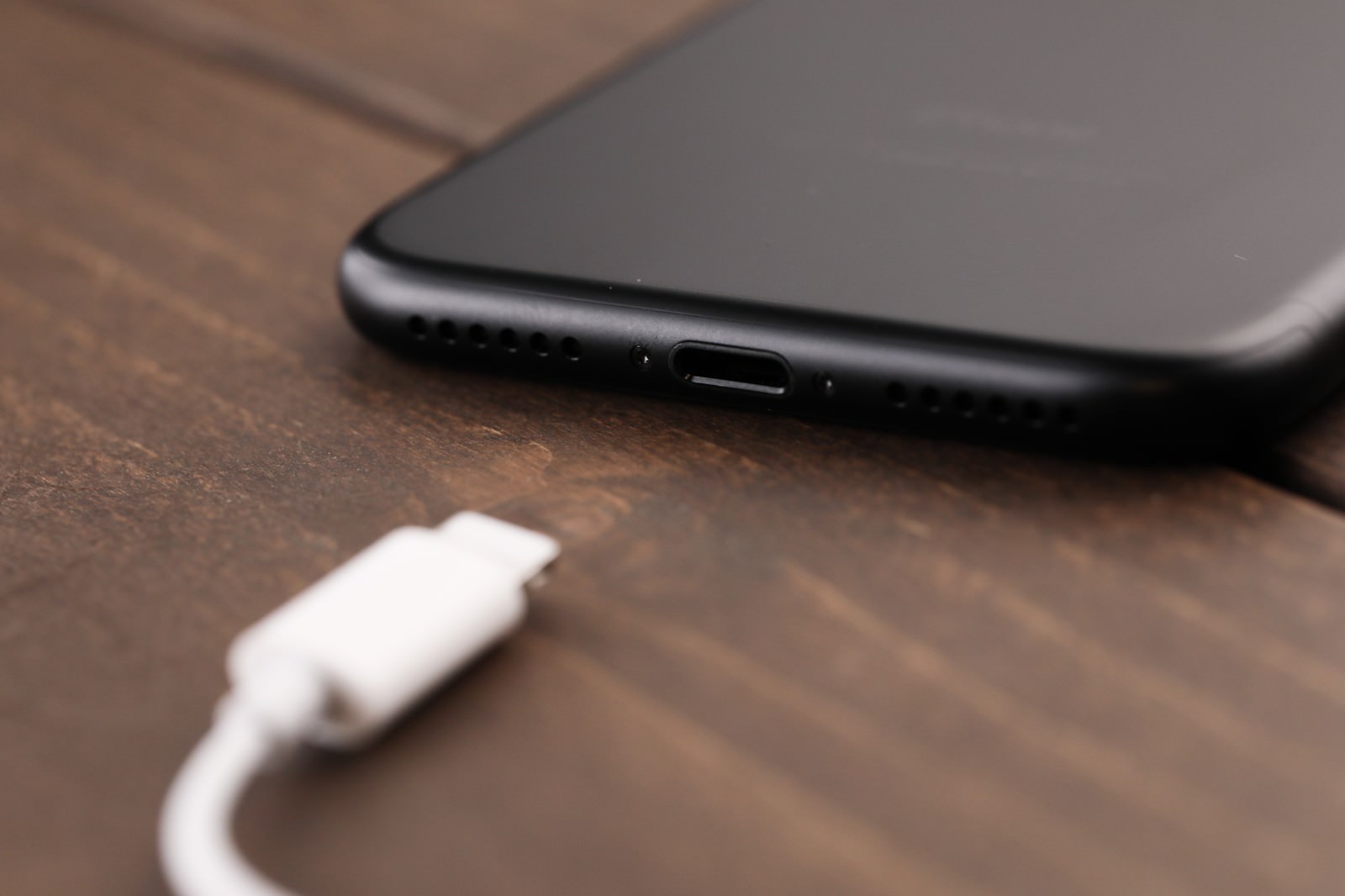 木目テーブルの上に置かれた黒いスマートフォンと白い充電コネクタ