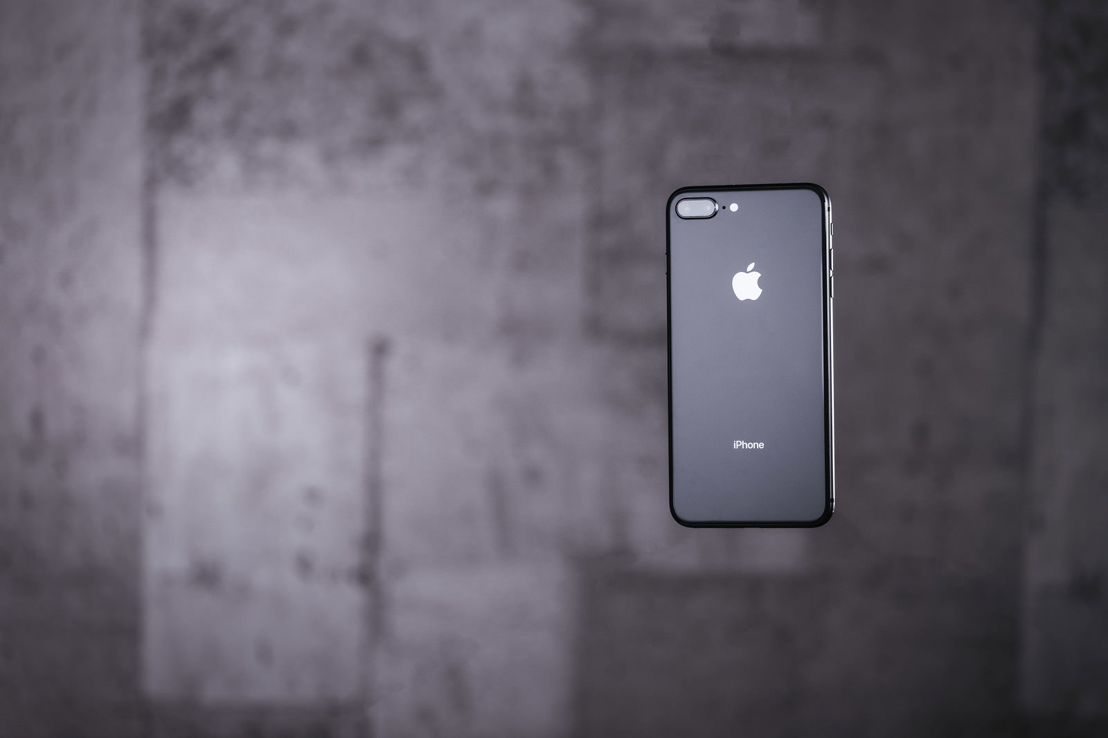 コンクリート壁の前に浮いたiPhoneの背面
