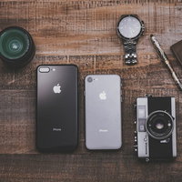 木目のテーブルに置かれた最新スマホとカメラやレンズの所持品の写真