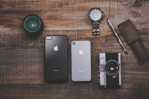 木目のテーブルに置かれた最新スマホとカメラやレンズの所持品