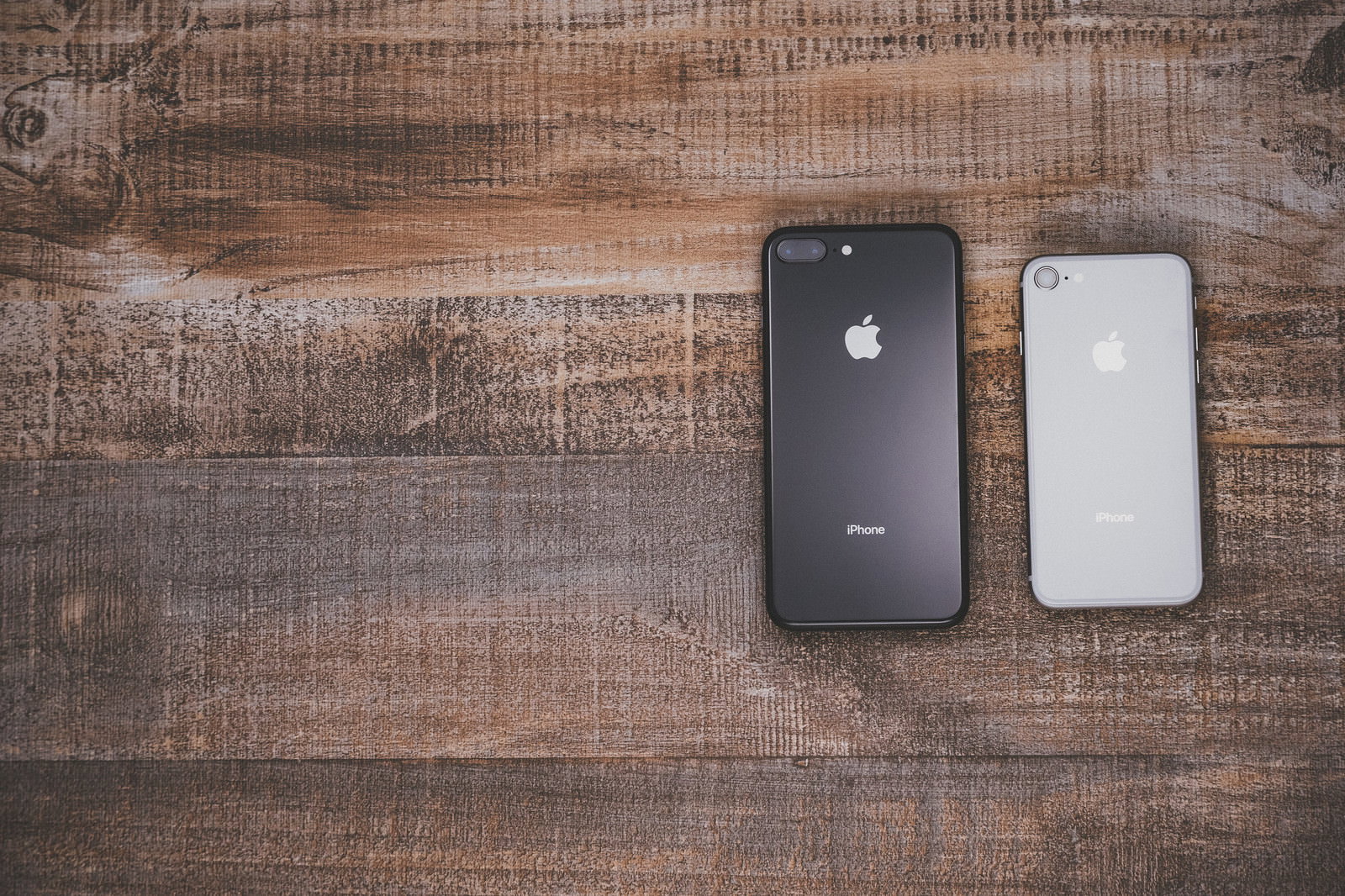木製テーブルの上に置かれたiPhone 8 PlusとiPhone 8の背面
