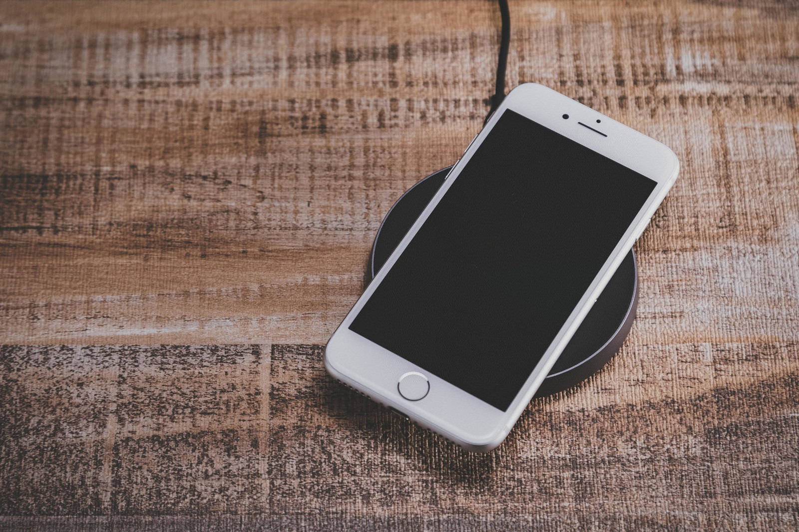 木目のテーブルの上でワイヤレス充電中のiPhone