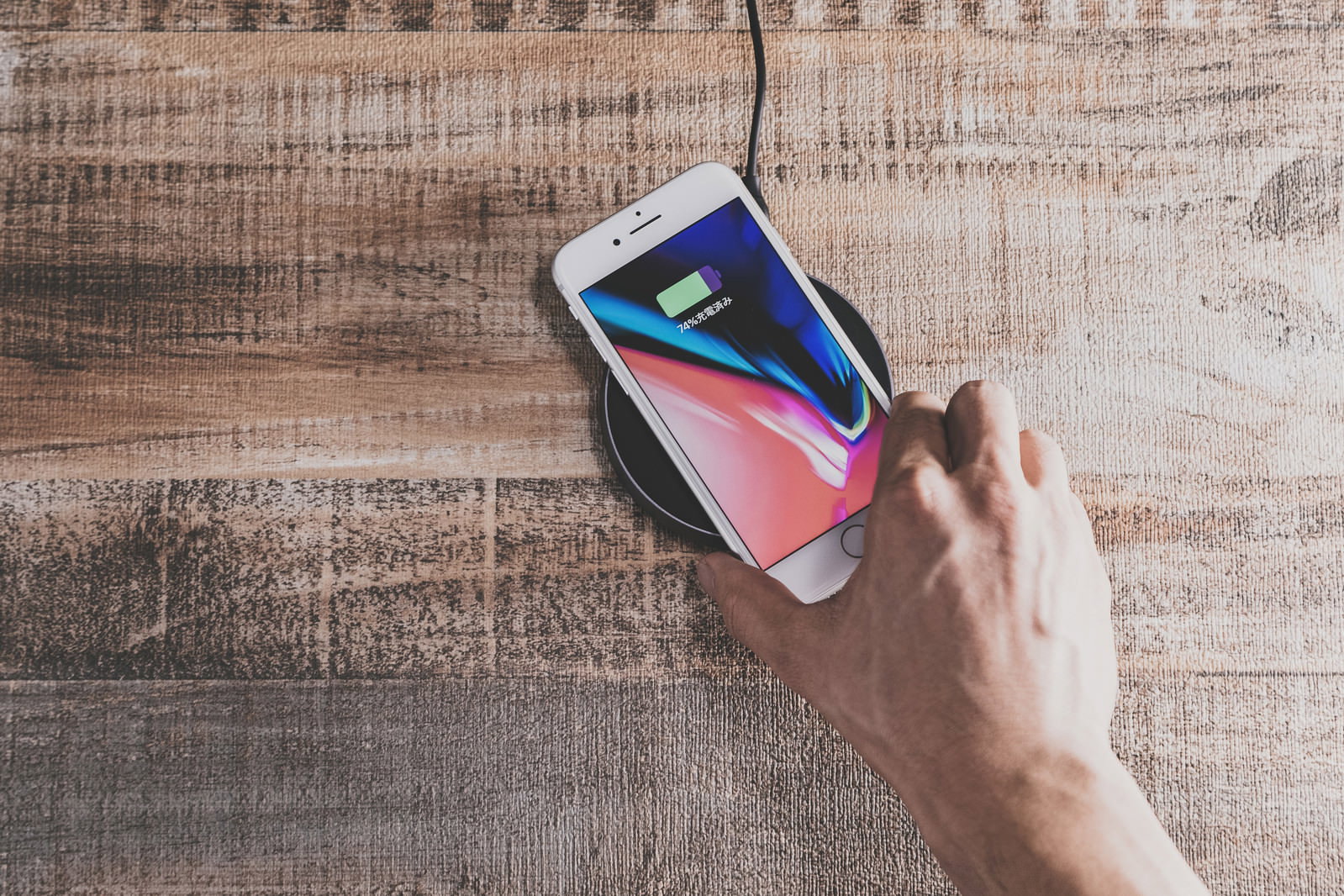 木目調の背景でワイヤレス充電パッドの上のiPhone 8に手が触れている