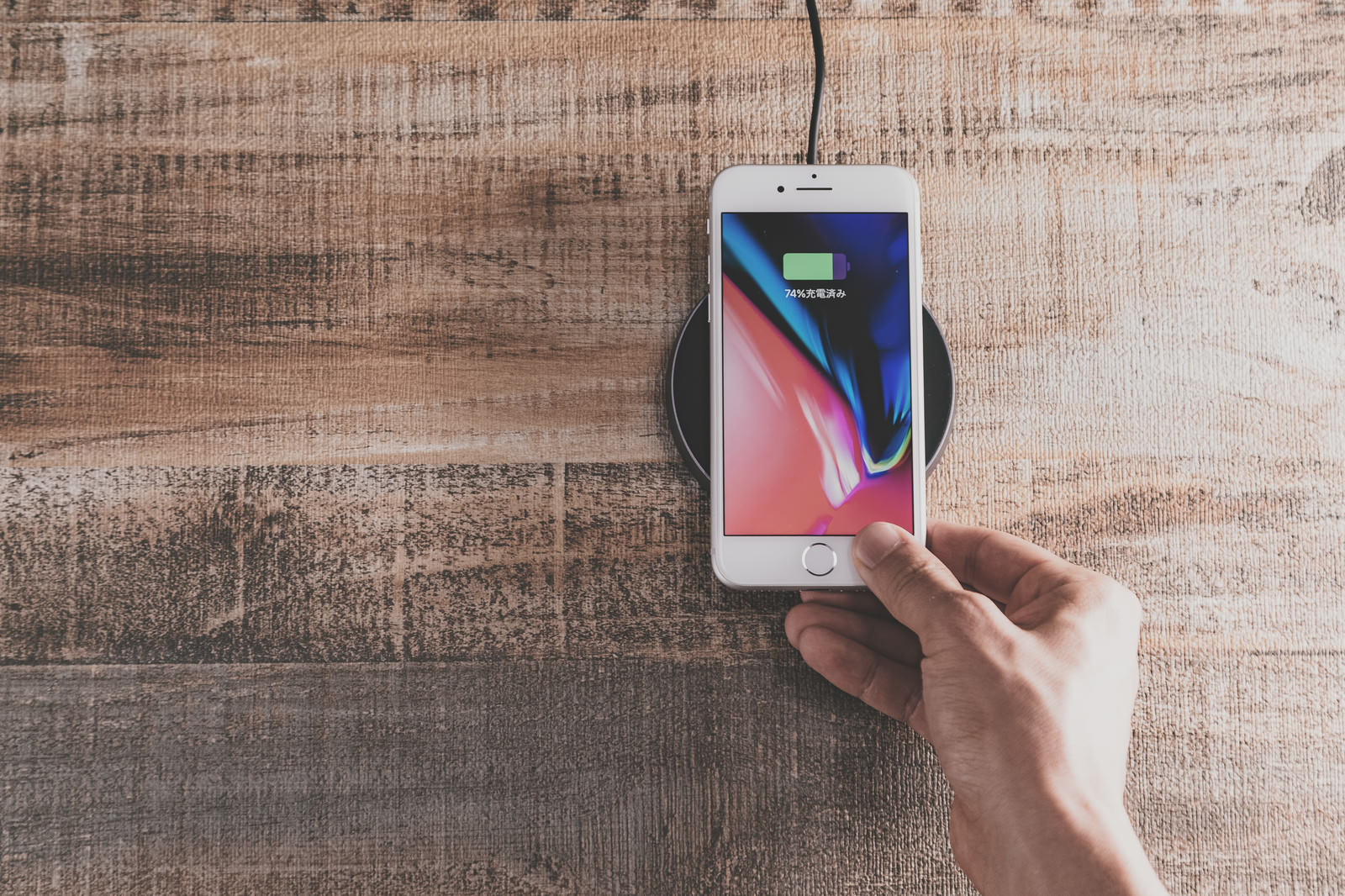 木製テーブル上のワイヤレス充電器でiPhoneを充電する手