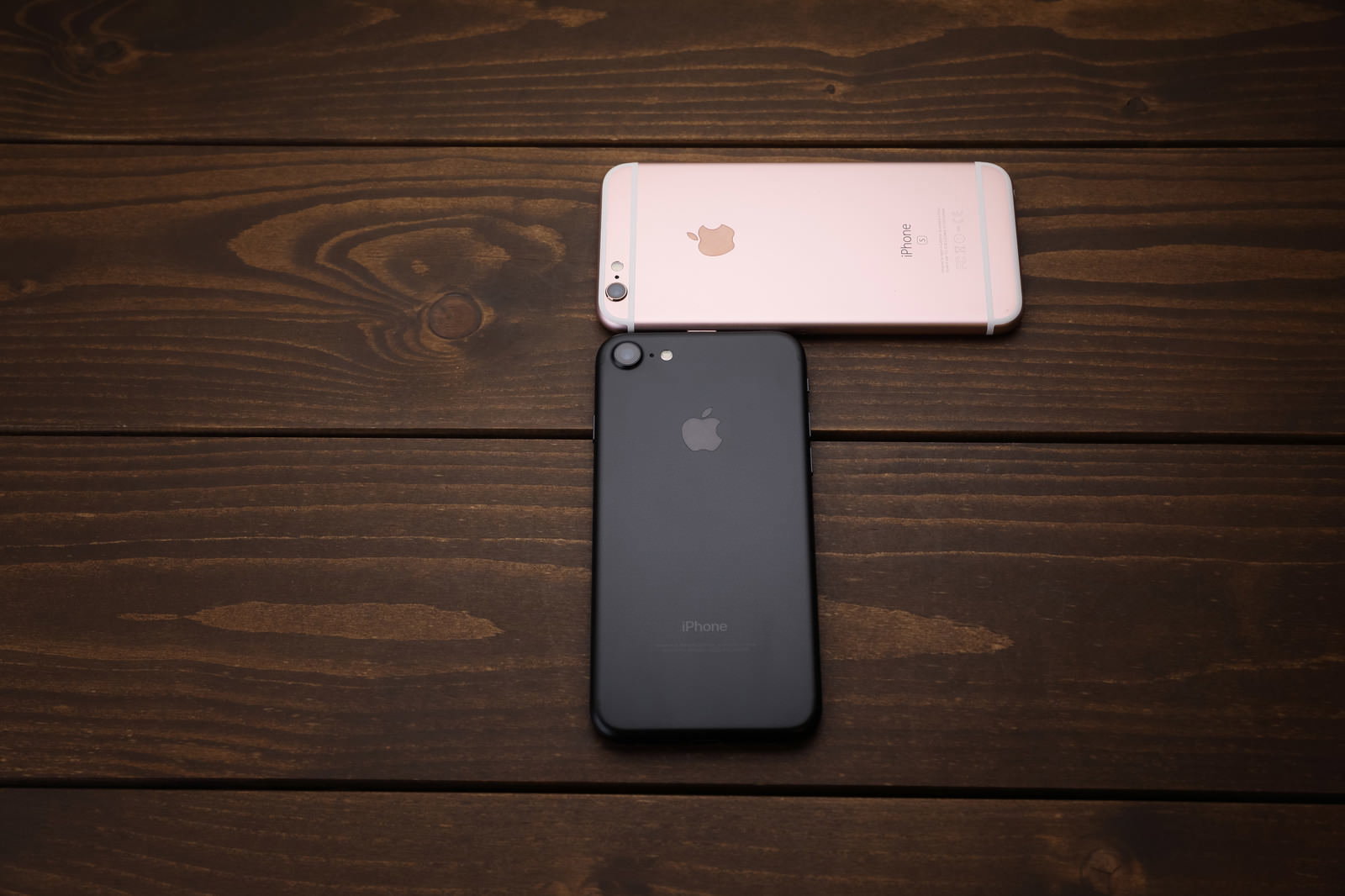 木製テーブルの上に黒とローズゴールドのiPhoneが2台並んでいる