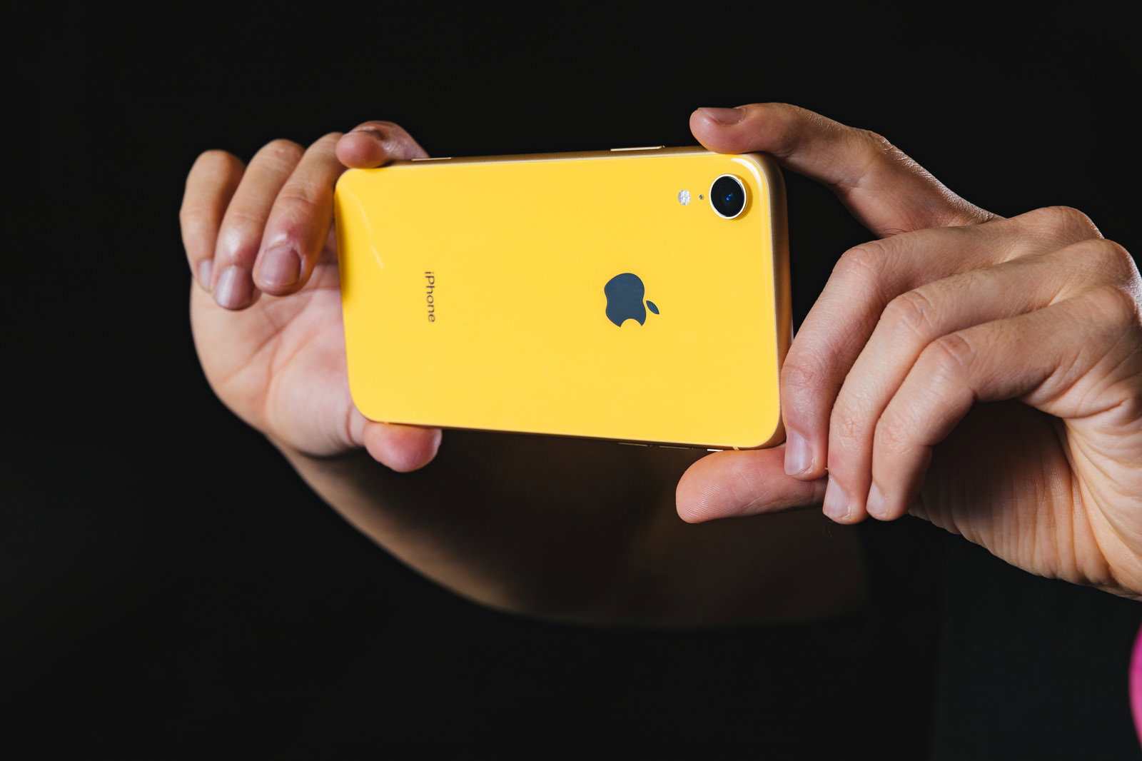 黄色いiPhoneを両手で持ってカメラ撮影している手元