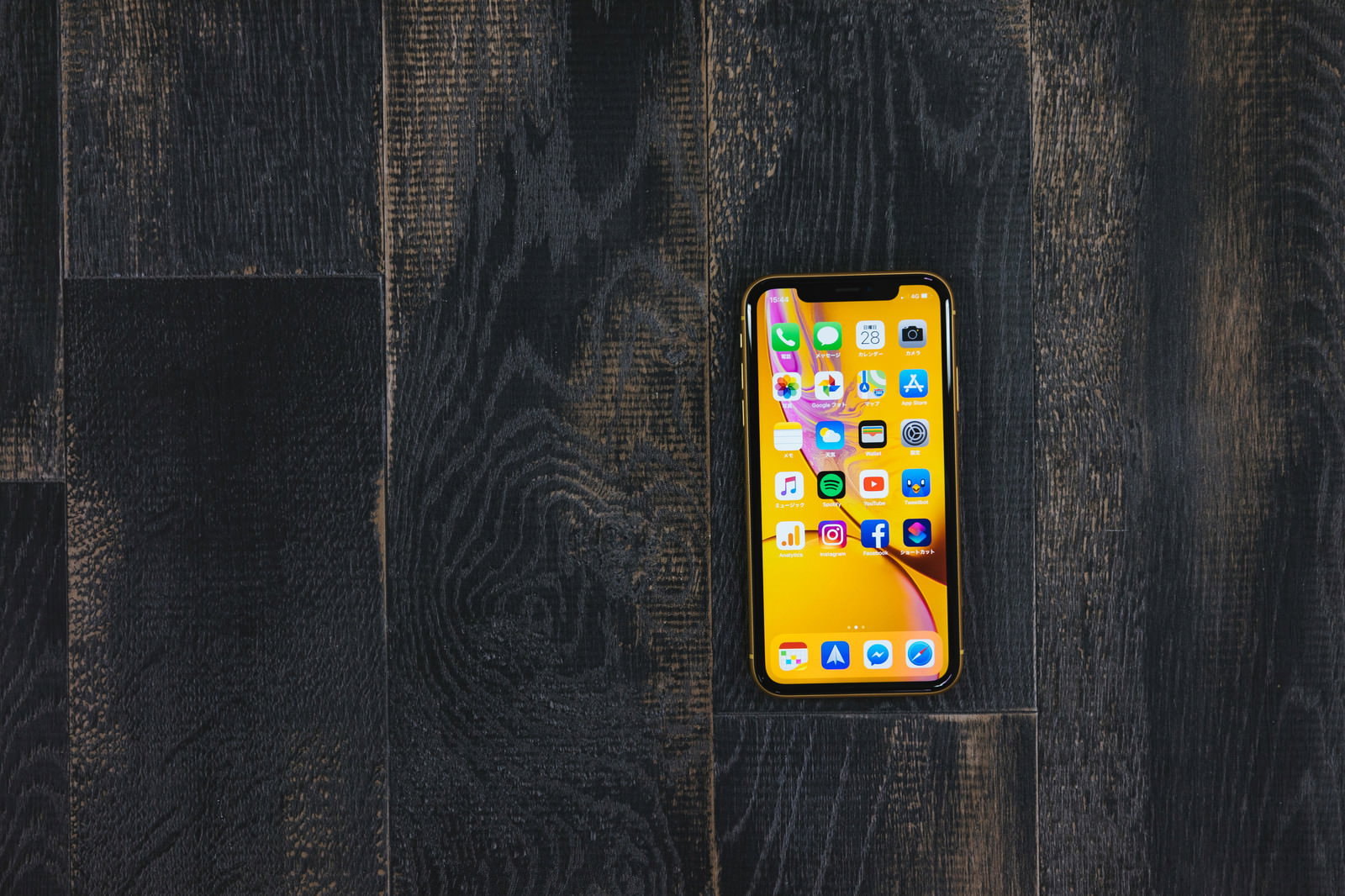 黒い木目テーブルに置かれたiPhone XRのホーム画面