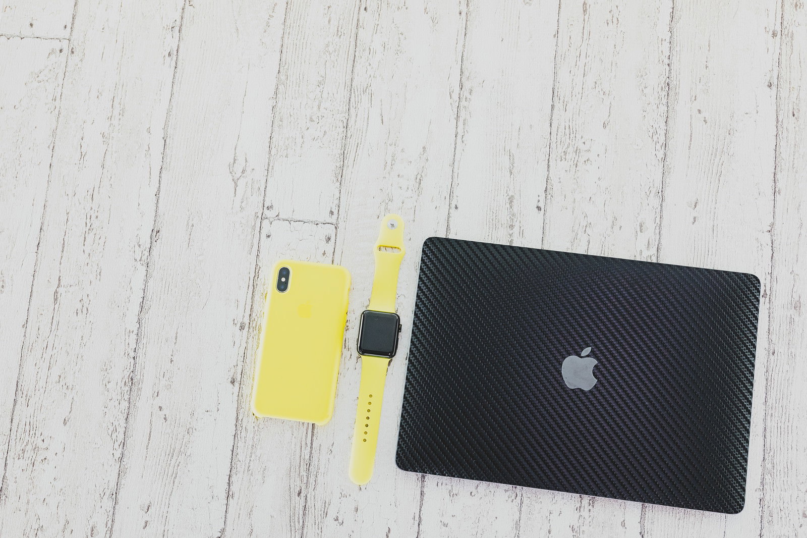 黄色ケースのiPhone・Apple Watch・黒いMacBookの俯瞰