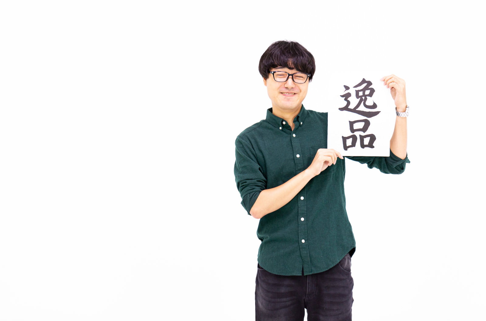 緑色のシャツを着た男性が笑顔で白い札を掲げている［モデル：真崎真幸］