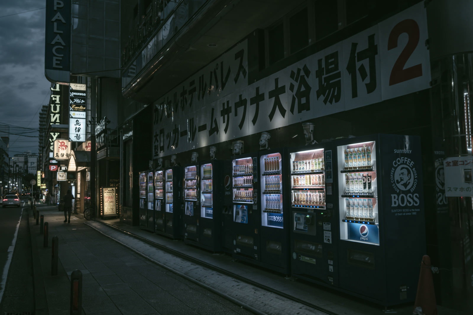 夜の歩道に明るく光る複数の自動販売機が並んでいる街並み
