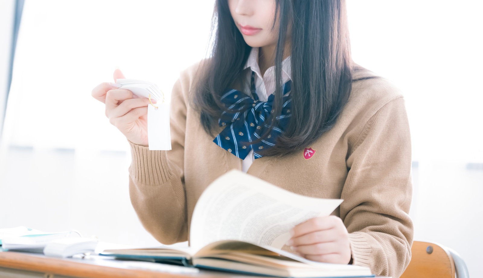 制服を着た女子高生が机に向かい単語カードを手に持って勉強している［モデル：石投げて美奈代］
