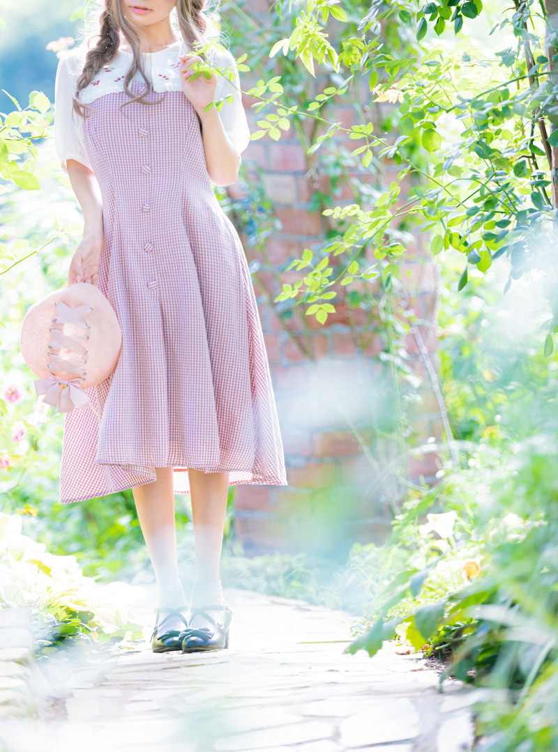 春の木漏れ日の中を淡い色のワンピースで散歩する女性［モデル：石投げて美奈代］